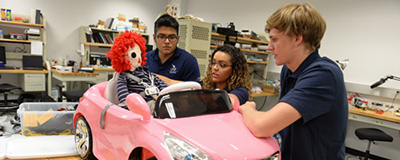 three students working on toy car