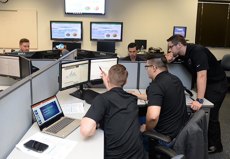 A group of UNF students in a room full of computers that have different data graphs on their screens