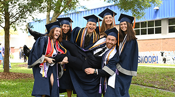 A group of students picking up their friend in caps and gowns