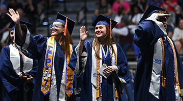 Students at commencement waving towards the crowd while walking towards their seats