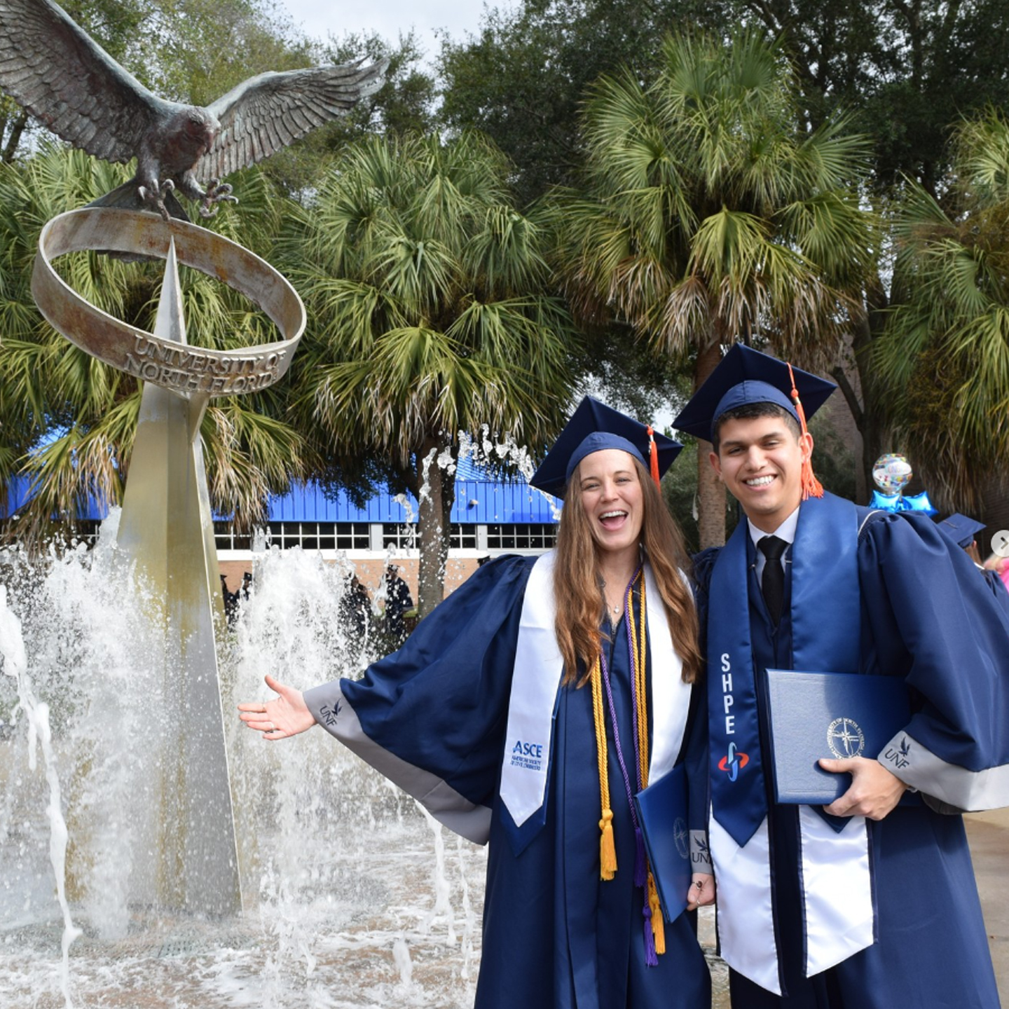 two students in their reglia with the osprey fountain next to them