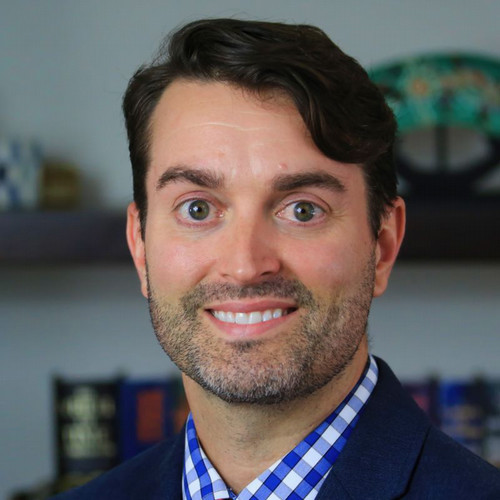 White male with short dark brown hair and green eyes smiling