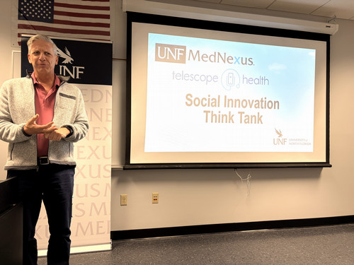 Man with gray jacket and red shirt standing with powerpoint slide