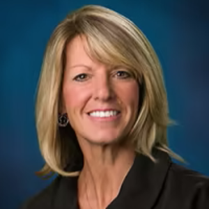 White woman with blonde hair black jacket with teal background