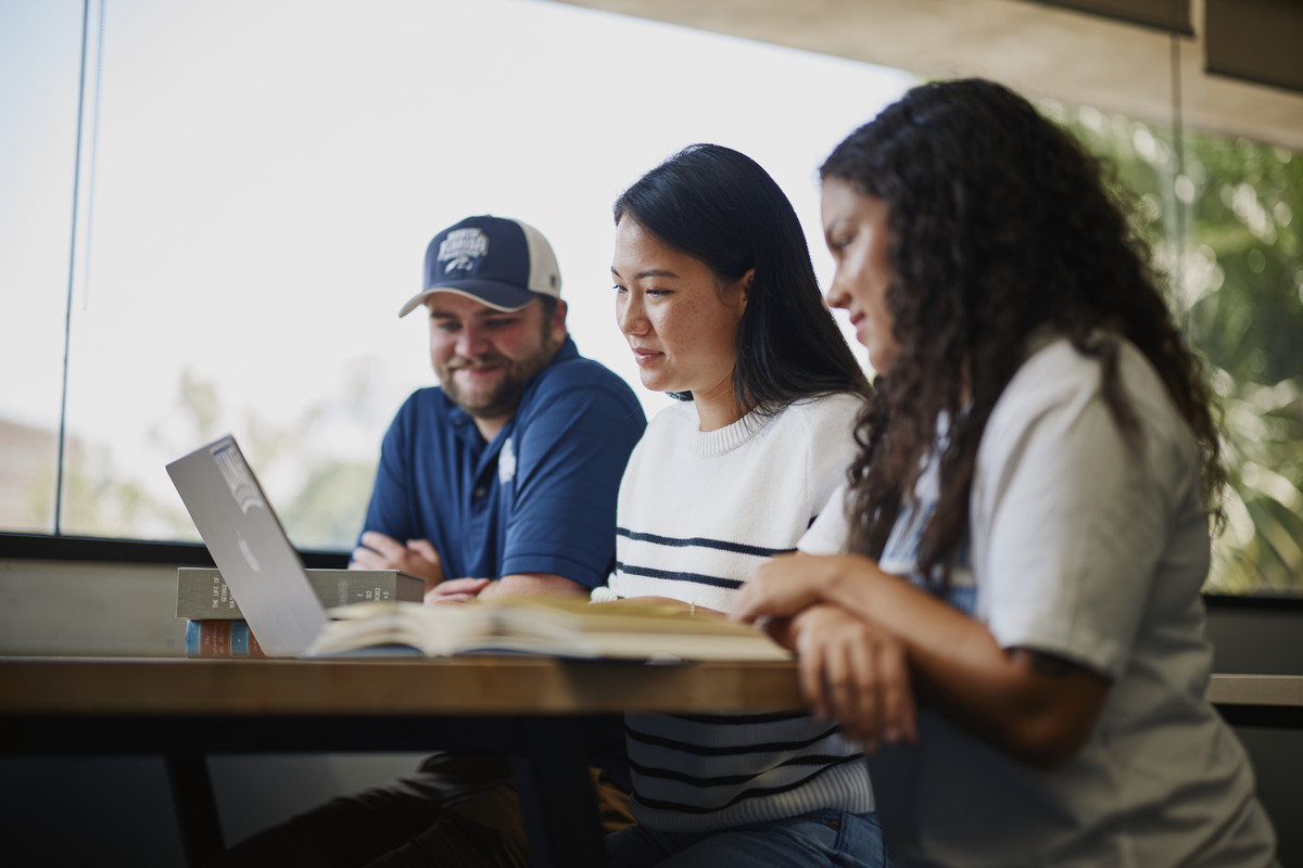 Three students sitting looking at laptop