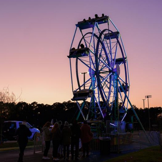 Blue ferris wheel in forefront. Sunset sky in background.