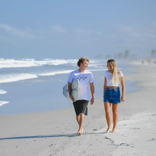 Two surfers walking on the beach and smiling at each other 