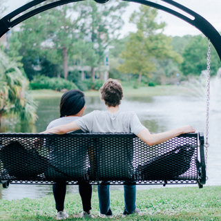 Two students sit on a bench in front of pond