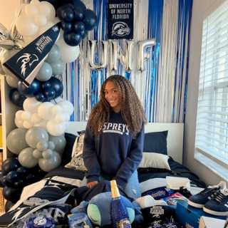 Girl kneeling on a bed, surrounded by UNF, blue, and gray themed decor