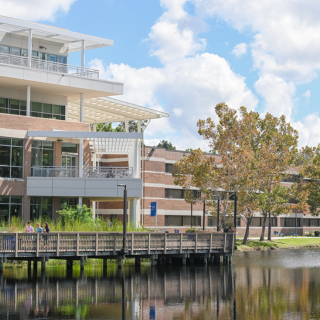 Photo with water in forefront, campus building in background 
