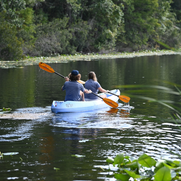 two students sitting in a blue kayak on a pond, nature surrounding them