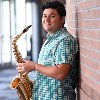student stands against wall with a saxaphone
