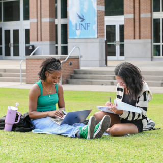 Two students sitting on grass, notebooks in front of them studying