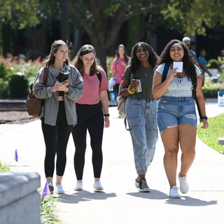 Four students walk on campus, smiling