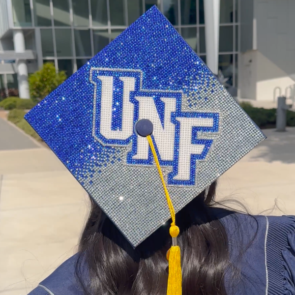A bedazzled graduation cap that is blue and silver and says "UNF"