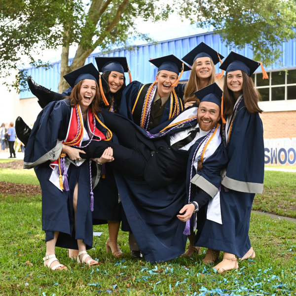 6 students in graduation regalia laughing in a group