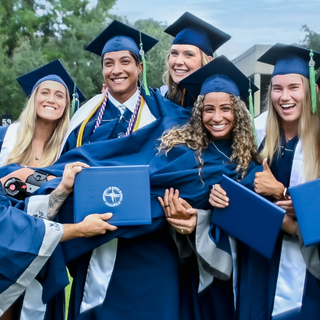 Students in a group smile and hold up diplomas