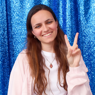 student smiles and holds up peace sign in front of blue background