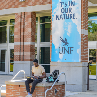 Student sits down with a computer in his lap. Above him is a blue sign that reads "It's in our nature" 