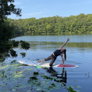 Student doing a yoga pose on a  paddle board surrounded by water