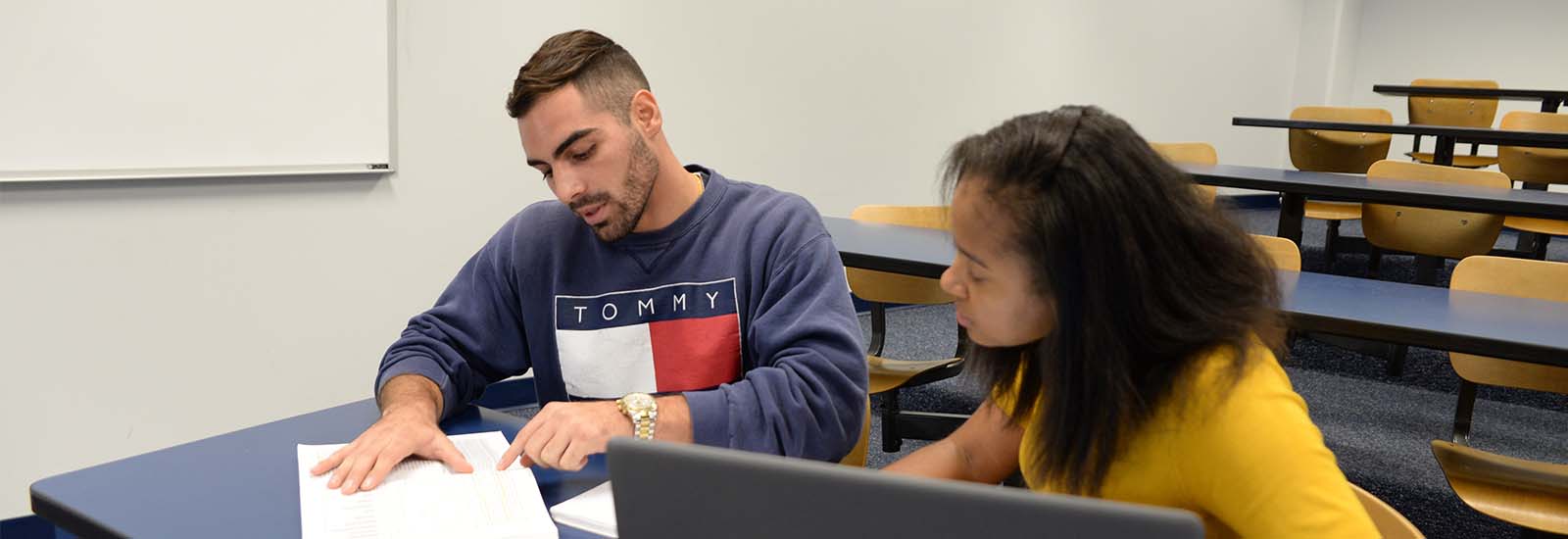 two students sitting in a classroom looking at a notebook