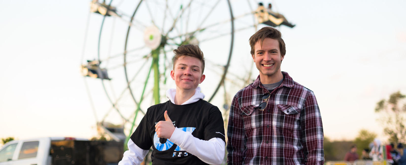Two male students smiling with a ferris wheel in the background at OZ Fest