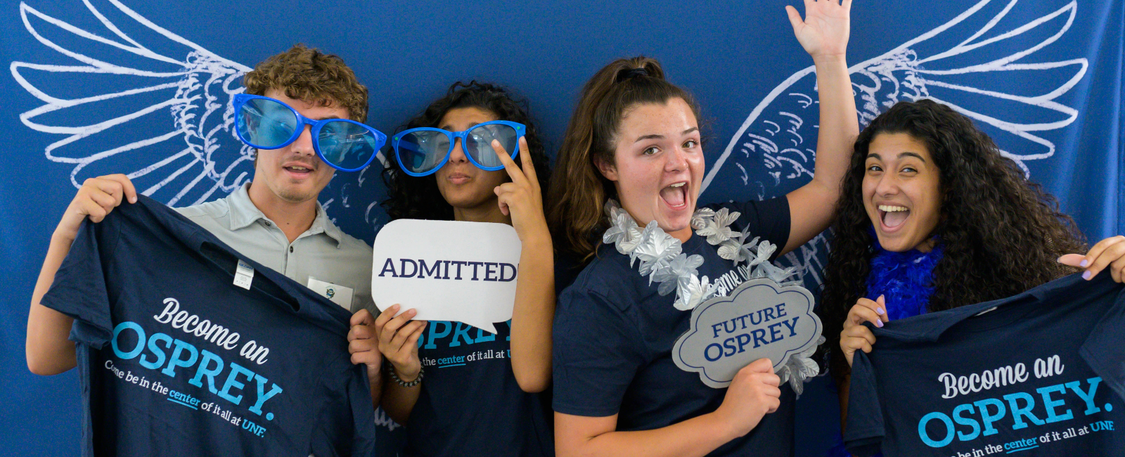 Four new UNF students in a photo booth holding UNF signs and striking crazy poses
