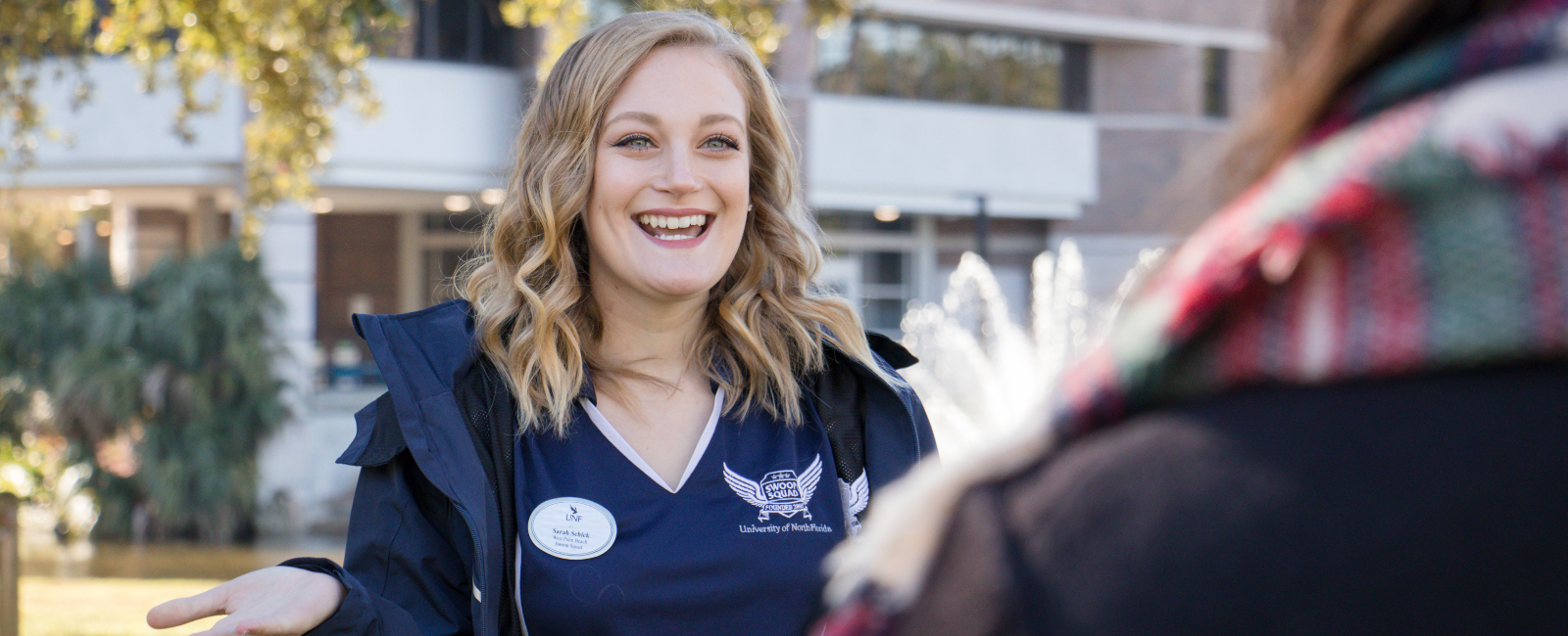 Female student worker in UNF branded clothing smiling while outside