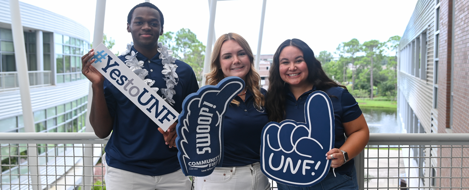 Three admissions counselors holding UNF foam fingers and smiling while standing outside