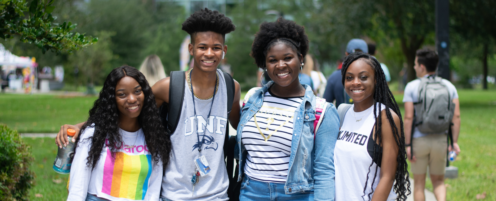 Four students standing outside on campus with their arms around one another smiling