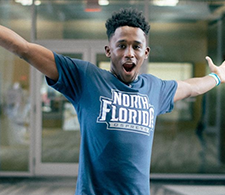 Male student in a UNF t-shirt holding his arms out with button text Secure Your Spot at UNF