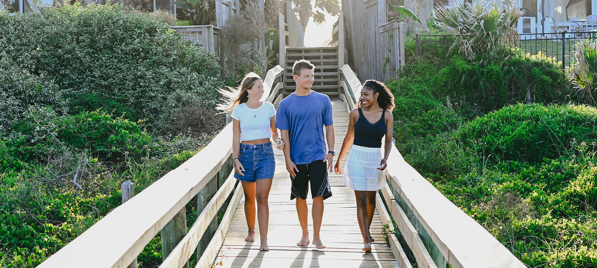 three students at the beach walking on a bridge together while talking 