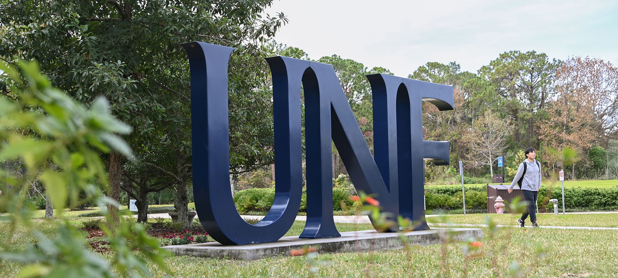 student walking by a UNF sign in the grass
