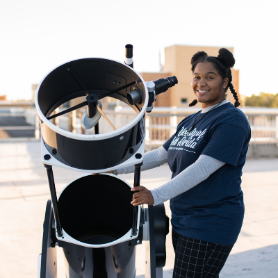 UNF student Kennedi Light standing by a telescope and smiling