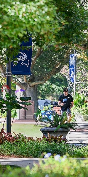 Student walking through campus surrounded by nature and UNF signs