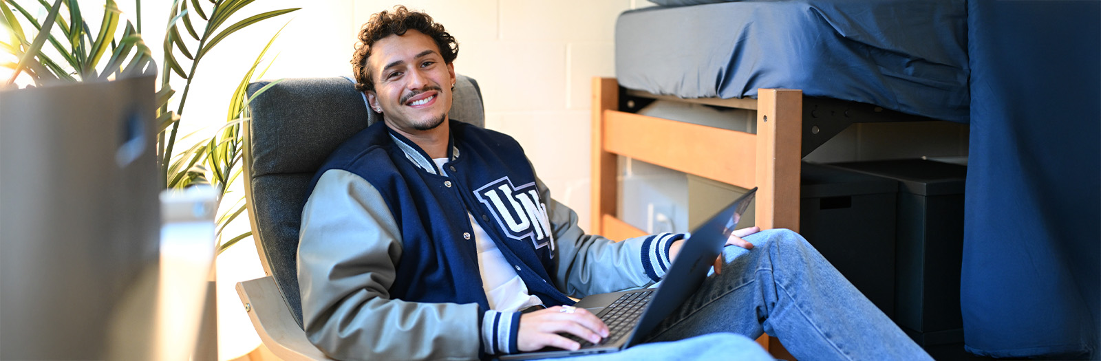A student sitting in a residence hall with a laptop