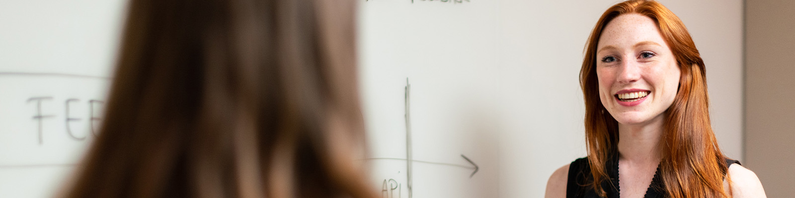 Redhead woman explaining something to a student in front of a whiteboard