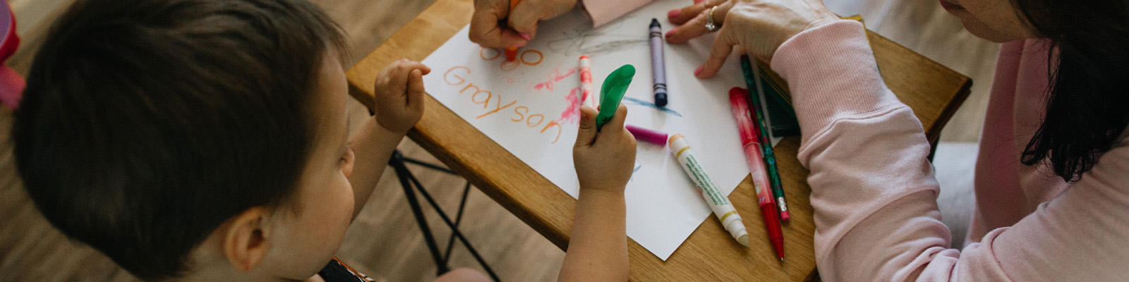 Teacher drawing on a piece of paper with a child using markers