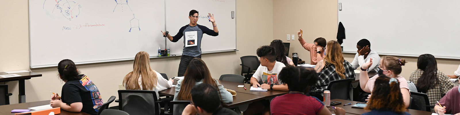 Student tutor in front of a whiteboard answering questions from seated students