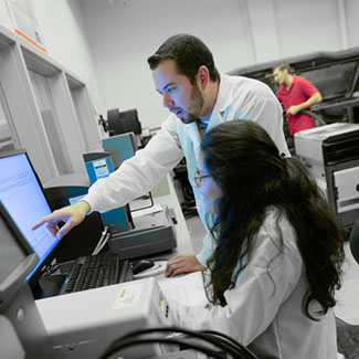 Two students in white labratory coats analyze data on computer screen