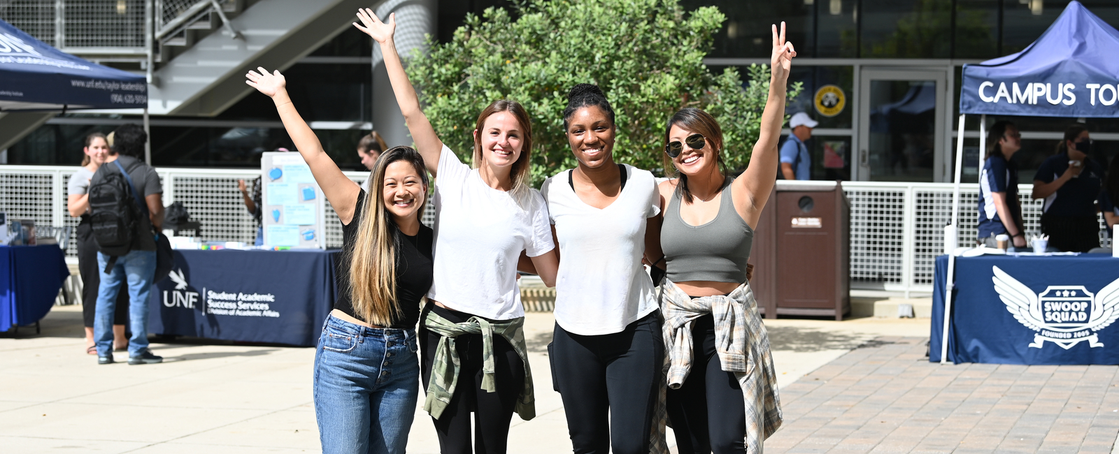 Group of four female students standing together with their hands up and smiling at the UNF student union