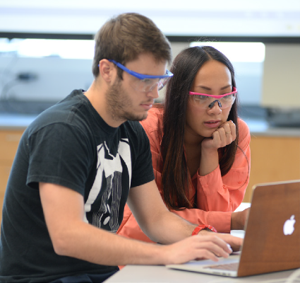 Male and female wearing safety glasses and looking at a computer