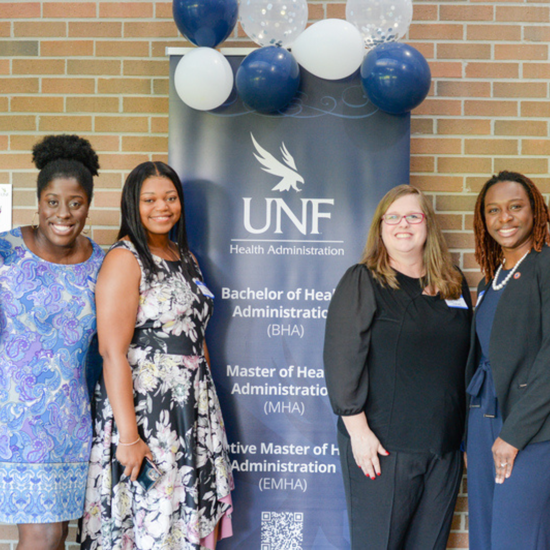 4 UNF MHA Students standing in front of a Health admin pop up poster