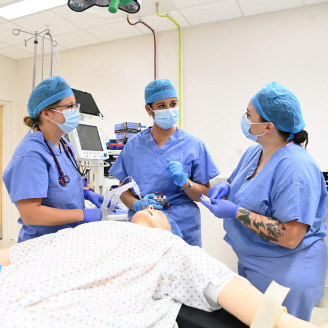Three nursing students in surgical attire with a mannequin