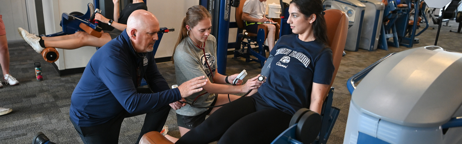 Kinesiology professor showing two students how to take a pulse measurement