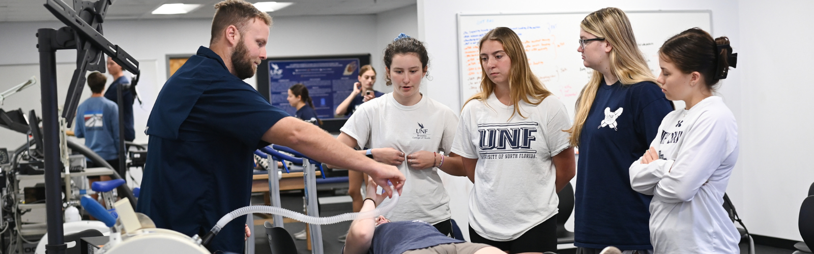 Kinesiology professor with five students, one is laying on a table holding a tube
