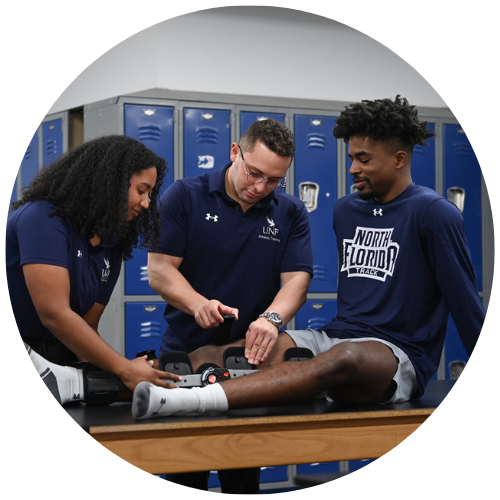 Three Athletic Training MS Students putting a leg brace on 