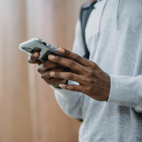 Man wearing gray hoodie and black backpack using his phone