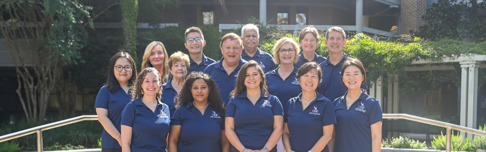 Health administration faculty and staff standing outside of the Brooks College of Health building as a group