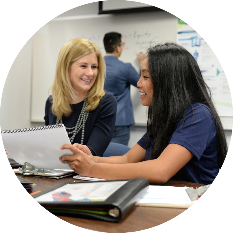 two health admin students talking while looking at a binder